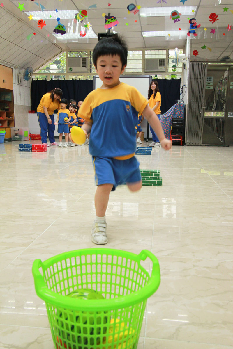 A child is throwing a bean bag into a basket