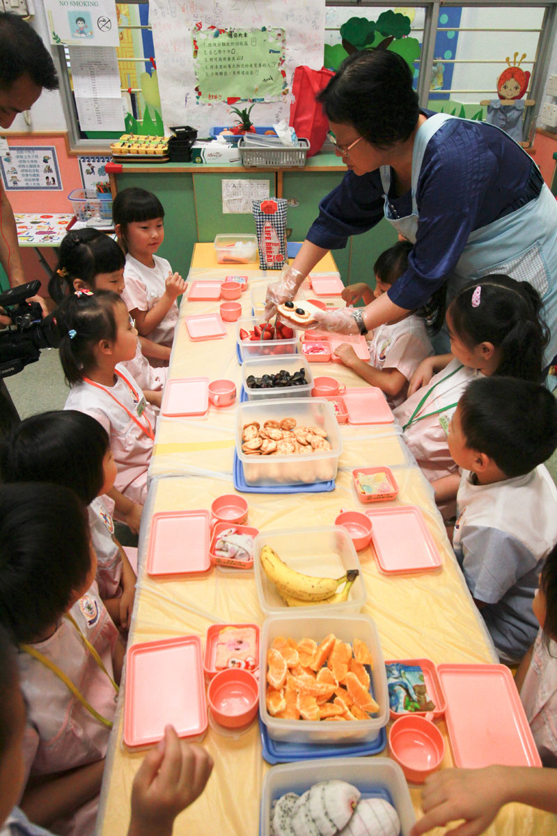 A teacher is distributing the food ingredients to the children