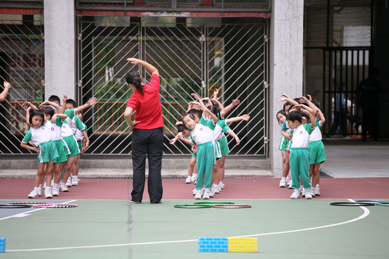 A teacher is instructing the children to do gymnastic exersice